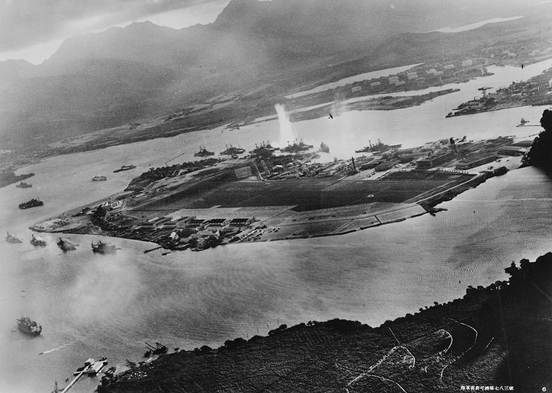 In a photo taken by a Japanese pilot, a plume of water rises from a torpedo that struck USS West Virginia (BB 48) moored on battleship row on the far side of Ford Island. A Japanese aircraft can be seen wheeling over the island, while another flies over the Navy Yard at the top right of the photo. Struck by six torpedoes and two bombs, West Virginia was salvaged, refitted, and took part in the Battle of Leyte Gulf in 1944 and was present for the signing of the Japanese surrender in Tokyo Bay on September 2, 1945. (US Navy)
